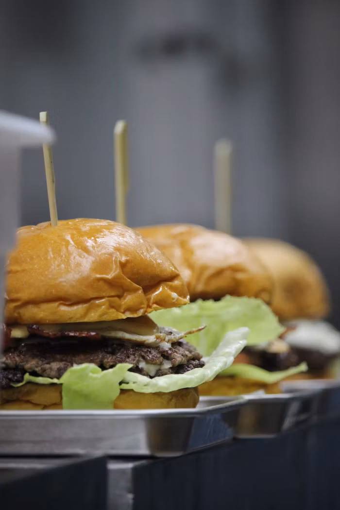 gallery-03 Close-up of fresh gourmet burgers with lettuce and cheese ready to serve.