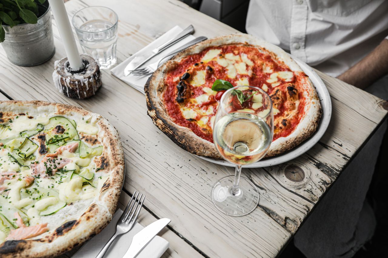 gallery-02 Appetizing pizzas with white wine served on a rustic wooden table, perfect for culinary enthusiasts.